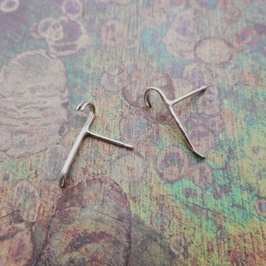 A photo of two miniature silver crowbars with ear-stud attachments.