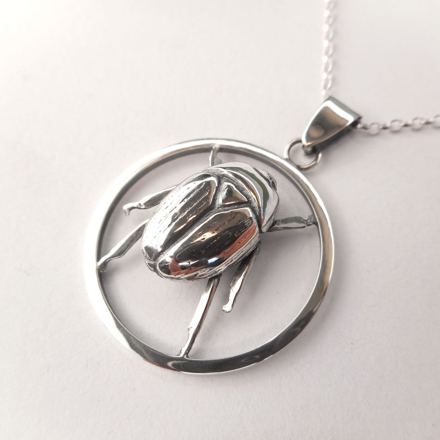 A photo of a silver pendant shaped like a scarab beetle in a hoop.