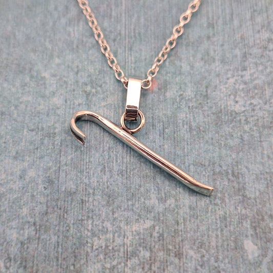 A photo of a silver pendant in the shape of a miniature crowbar, on a blue background.