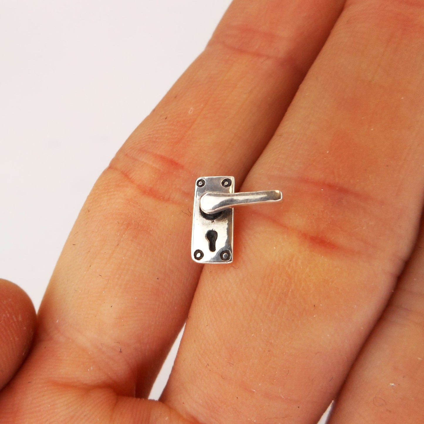 A photo of a miniature silver door handle, between two fingers of a hand.