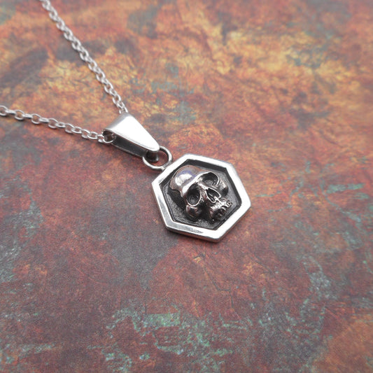 A photo of a silver skull pendant, on a mottled red background.