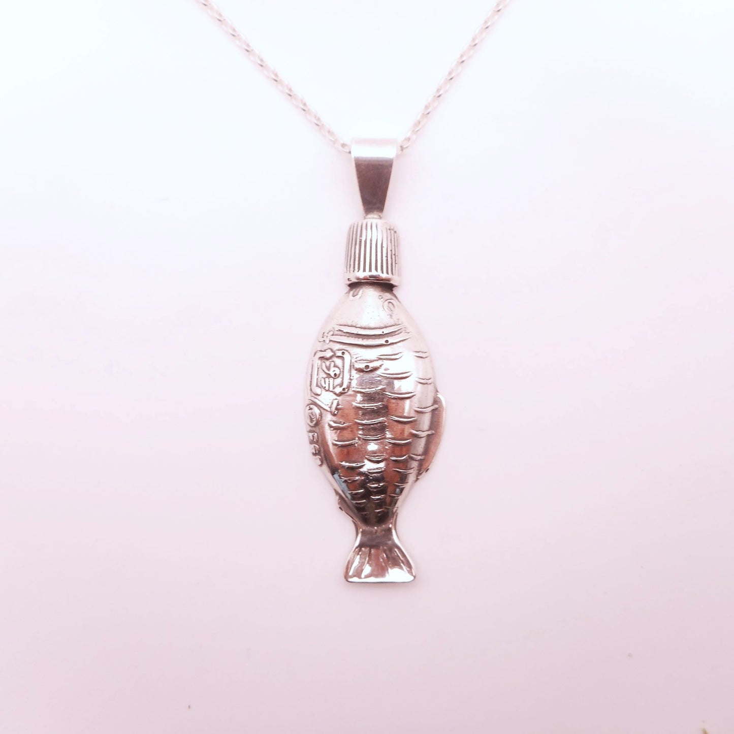 A photo of a soy sauce fish bottle made of silver, attached to a chain, on a white background.