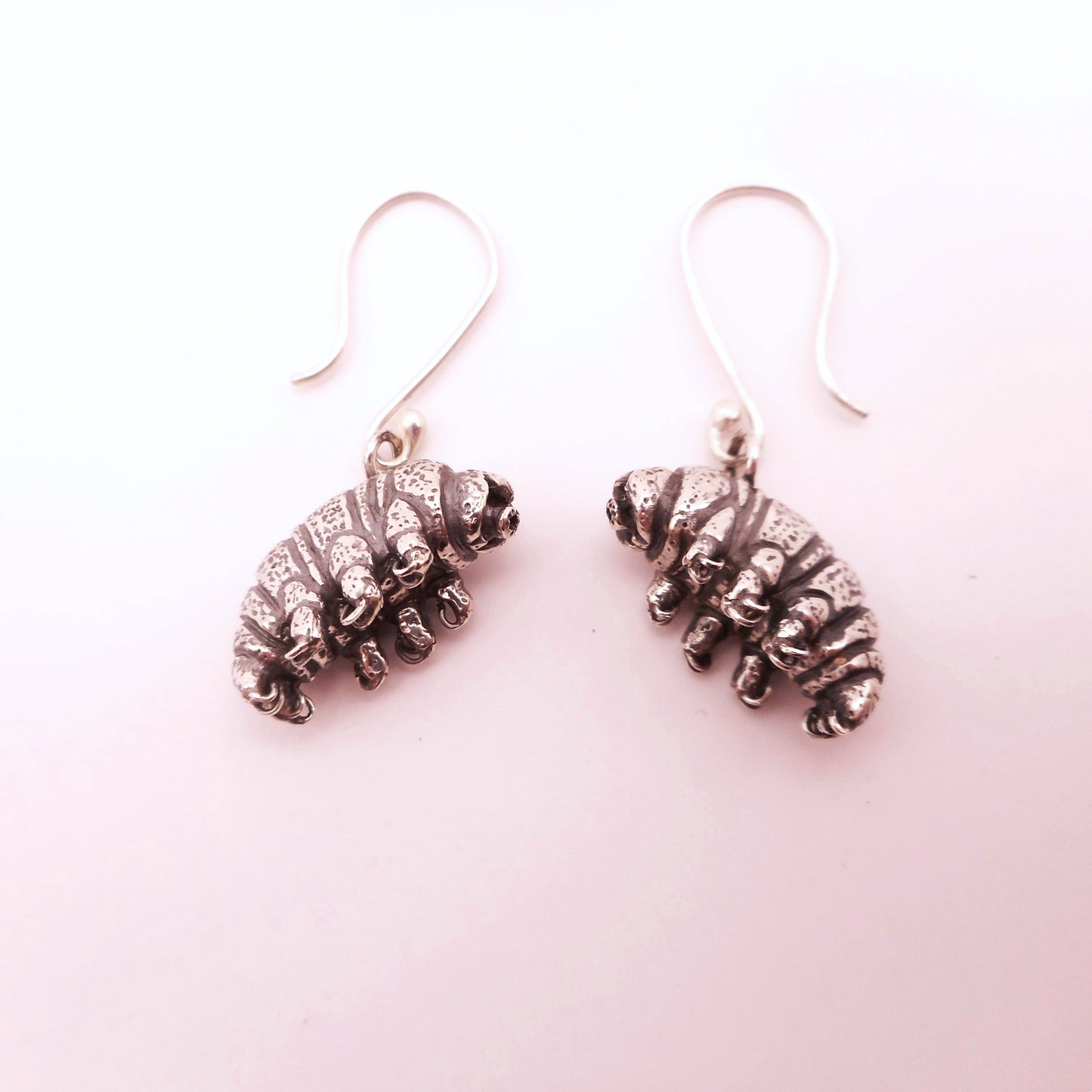 A photo of a pair of silver earrings shaped like tardigrades, on a white bakground.