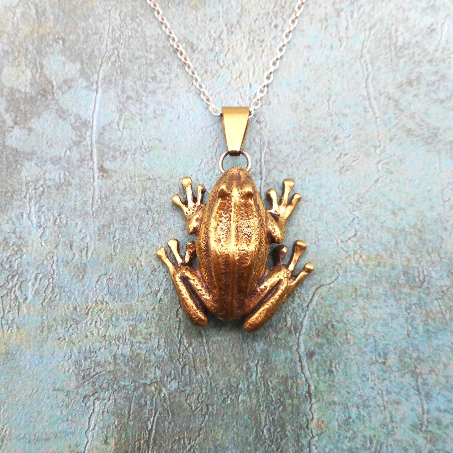 A photo of a brass frog pendant on a blue background.