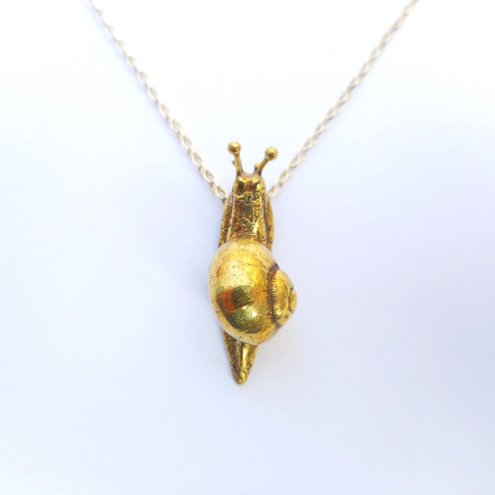 A photo of a brass snail, attached to a chain, on a white background.