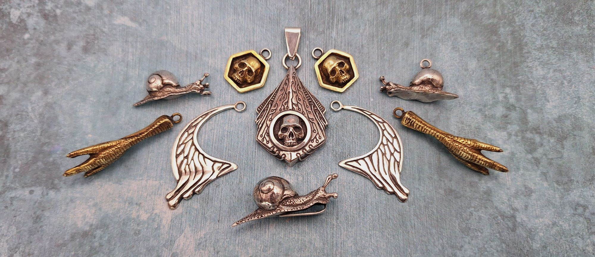 several pieces of unusual jewellery in the shape of skulls, snails and chicken feet, resting on a blue background.