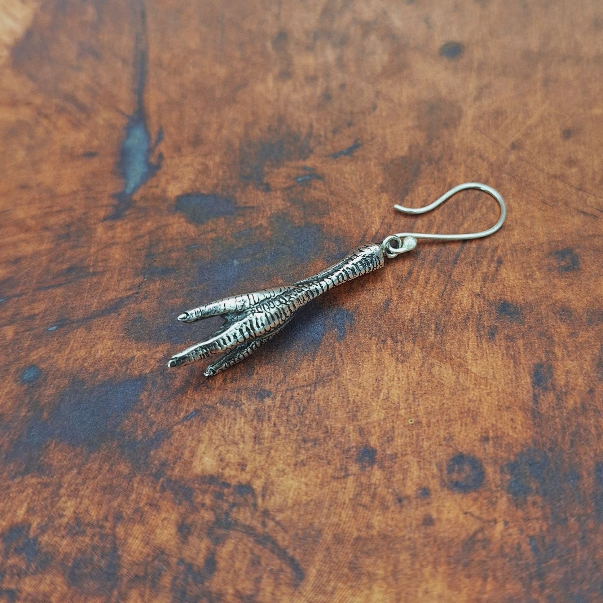 A photo of a silver earring in the shape of a chicken foot, on a red background.