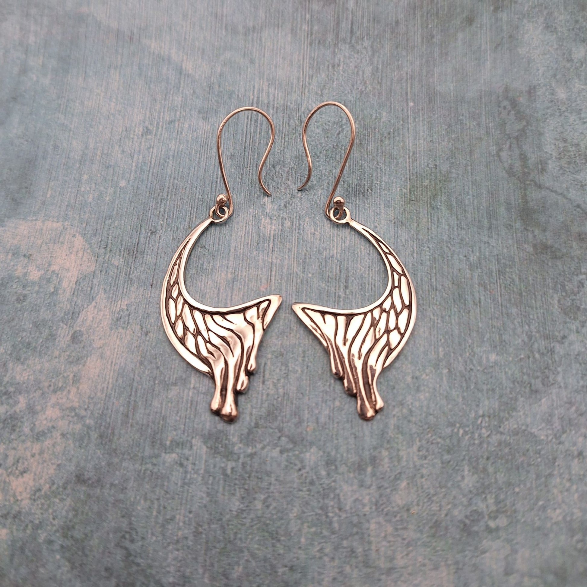 A photo of a pair of abstract crescent earrings, on a mottled blue background.