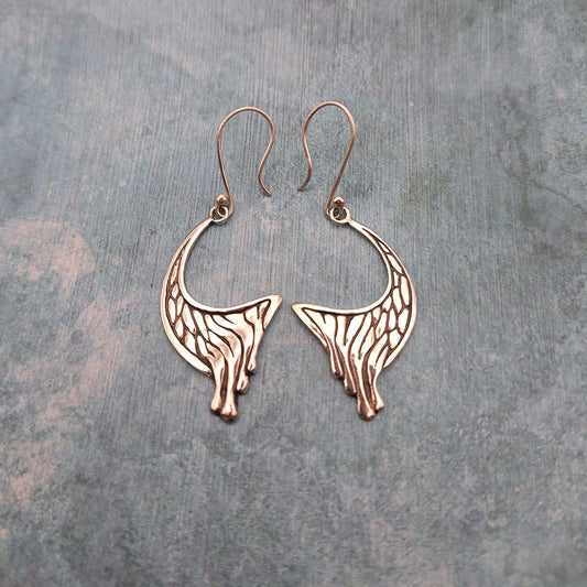 A photo of a pair of abstract crescent earrings, on a mottled blue background.
