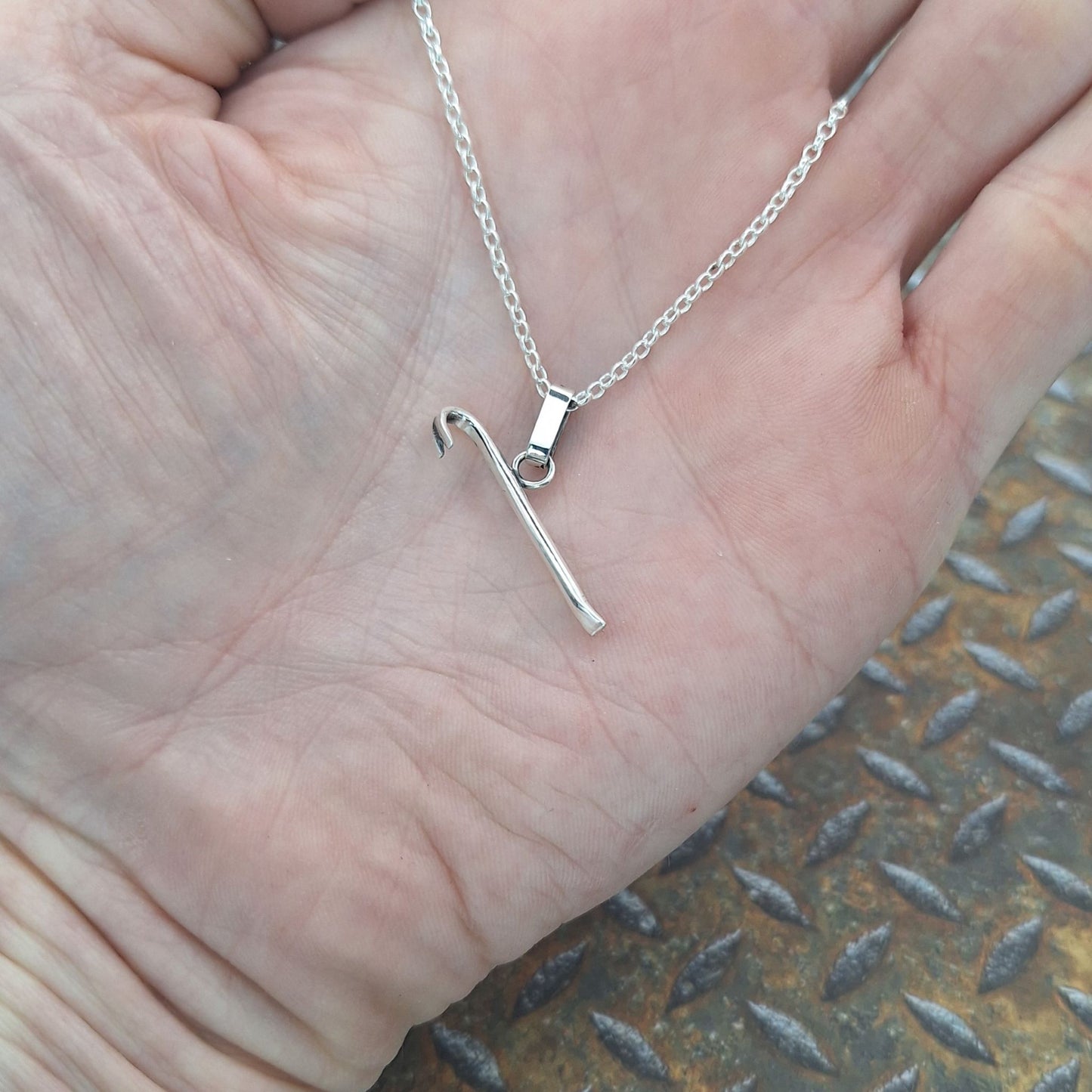 A photo of a crowbar necklace on the palm of a hand.