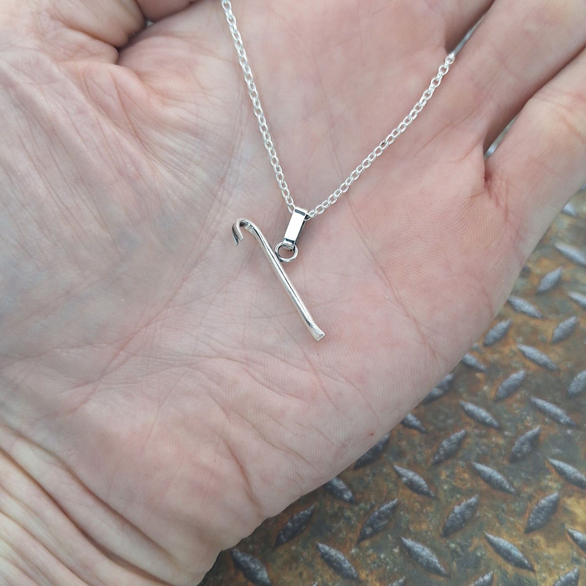 A photo of a crowbar necklace on the palm of a hand.