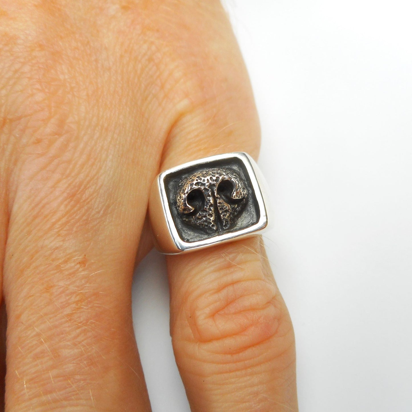 A photo of a silver ring in the shape of a dog's nose, one the little finger of a hand, on a white background.