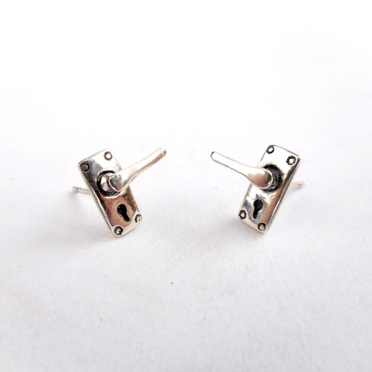 A photo of a pair of silver ear studs, in the shape of miniature door handles, on a white background.