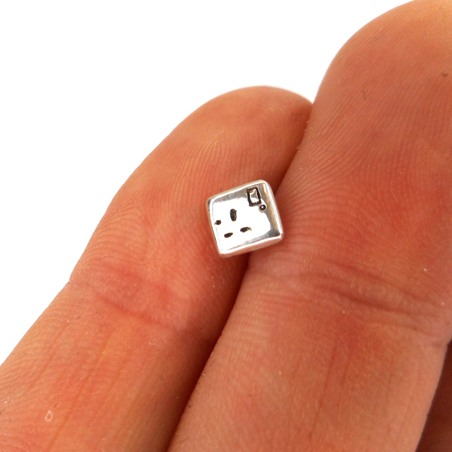 A photo of a miniature electrical outlet made of silver, on the fingers of a hand.