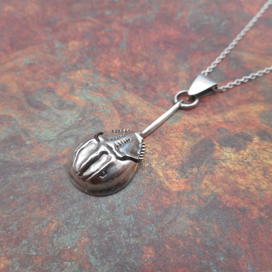 A photo of a silver horseshoe crab pendant, on a mottled red background.