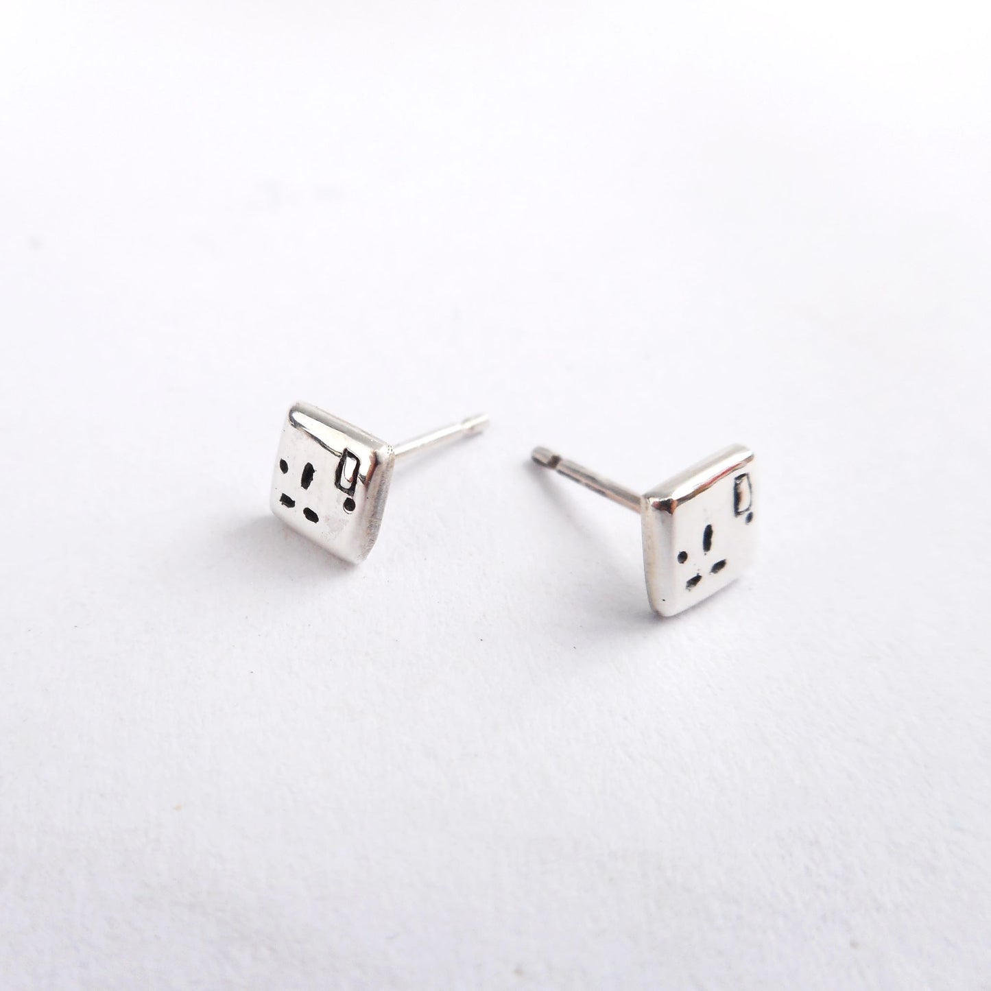 A photo of a pair of silver ear studs in the shape of plug sockets, on a white background.