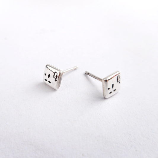 A photo of a pair of silver ear studs in the shape of plug sockets, on a white background.