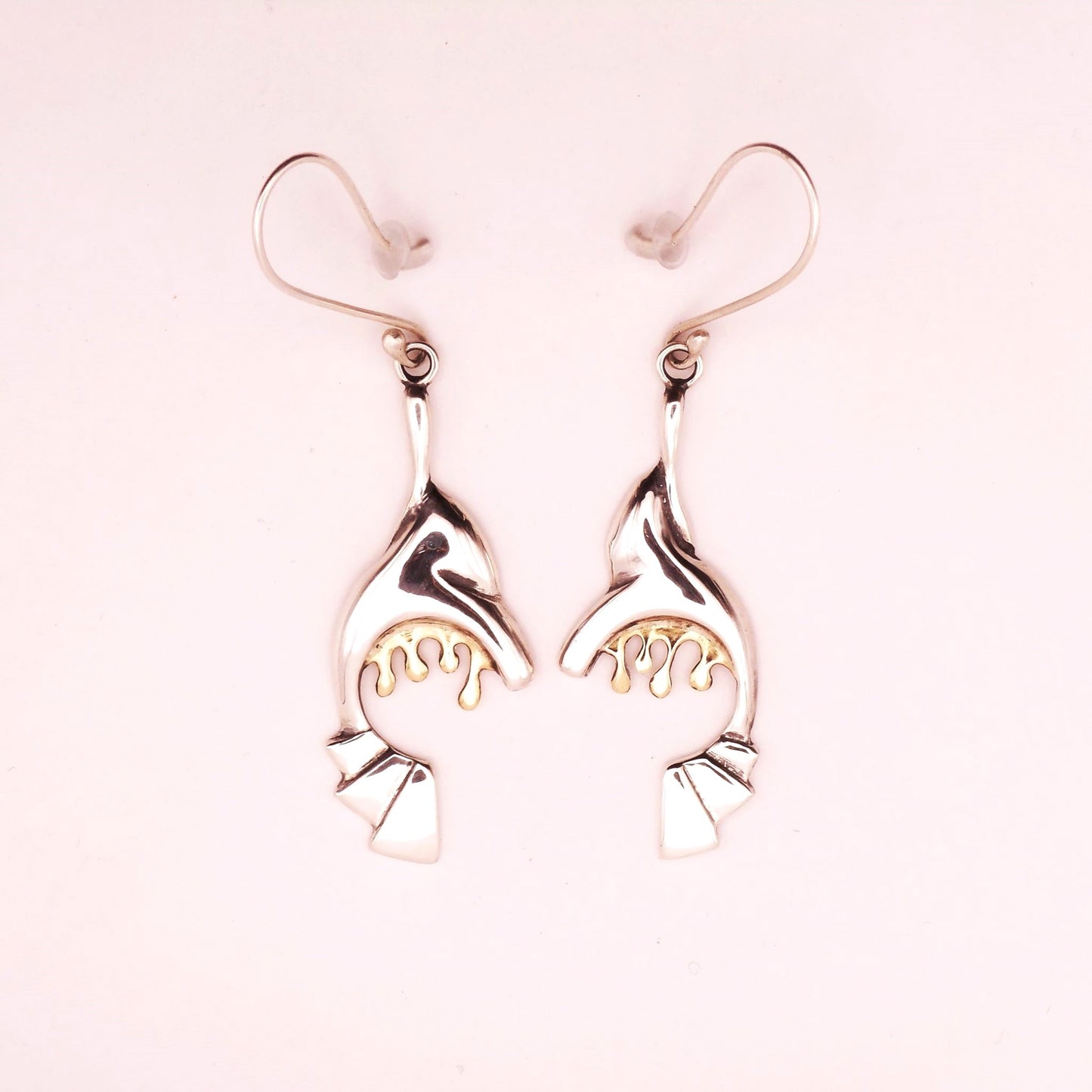 A photo of a pair of abstract silver earrings with golden drips hanging form them.