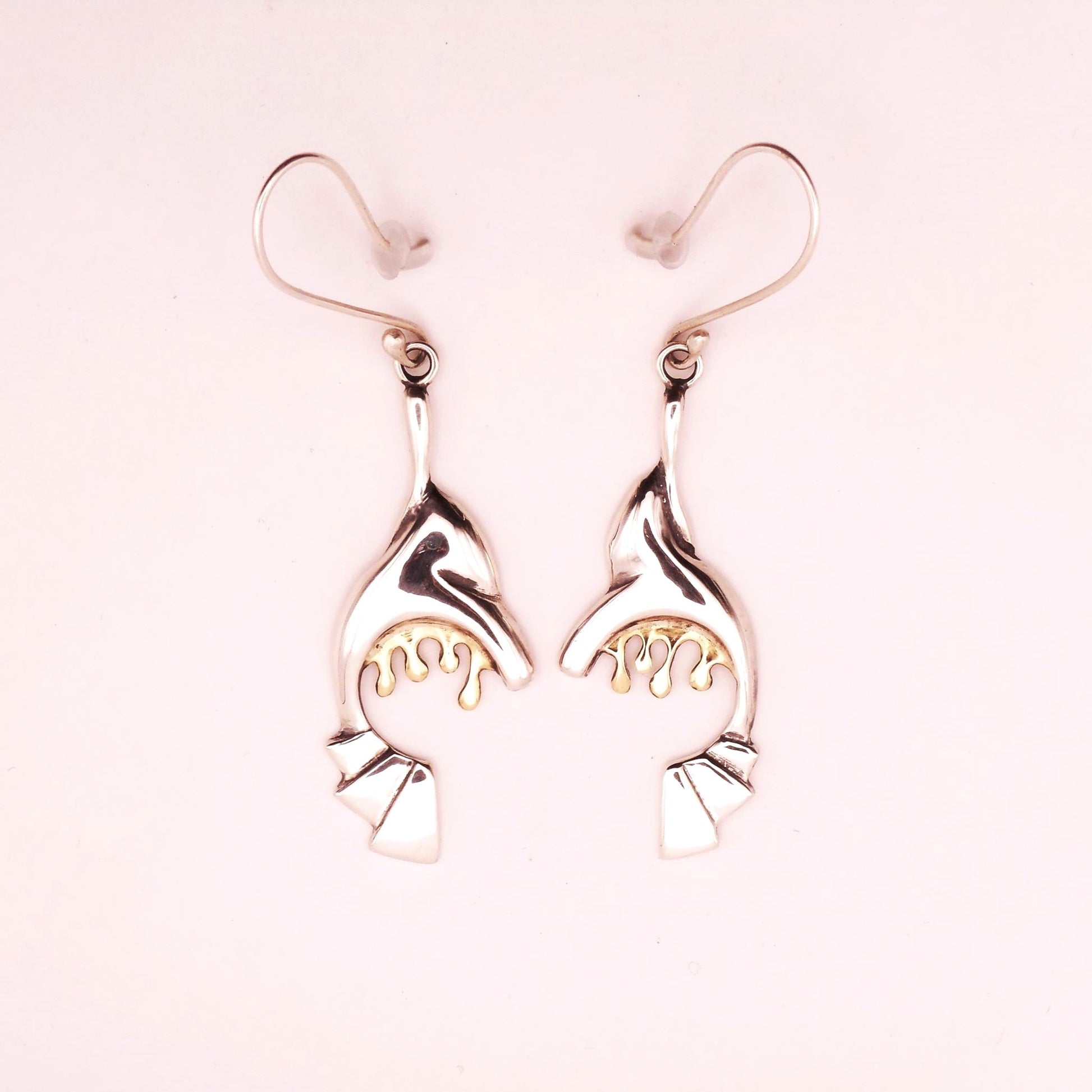 A photo of a pair of abstract silver earrings with golden drips hanging form them.