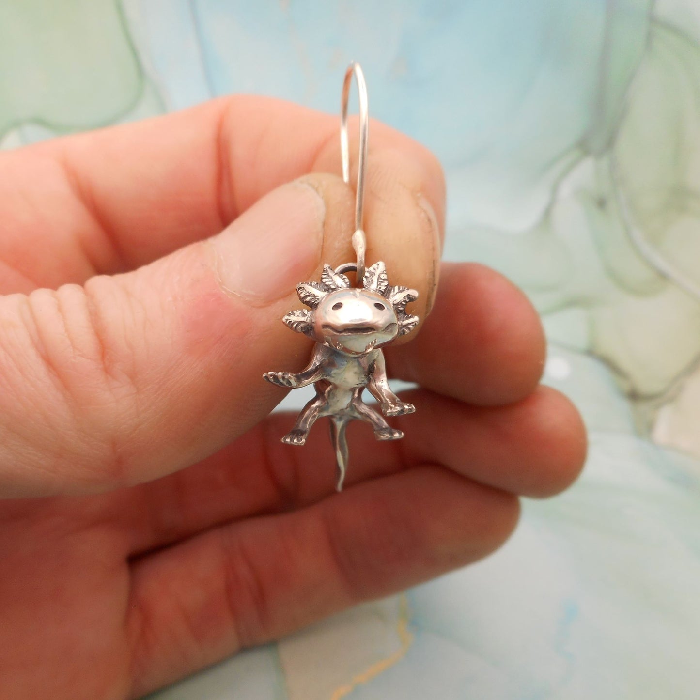 A photo of an axolotl earring held between thumb and forefinger.