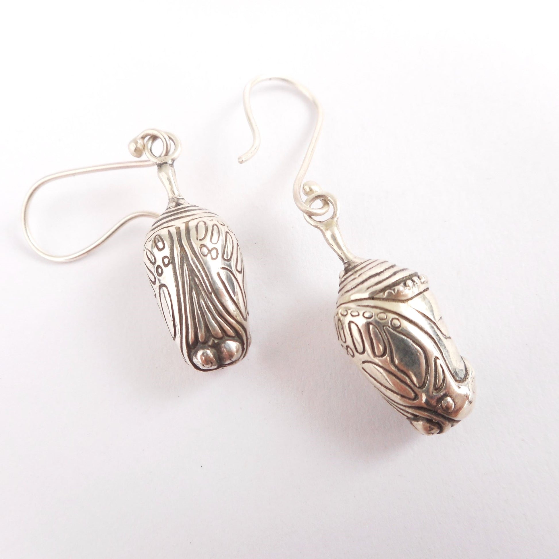 A photo of a pair of silver chrysalis earrings on a white background.