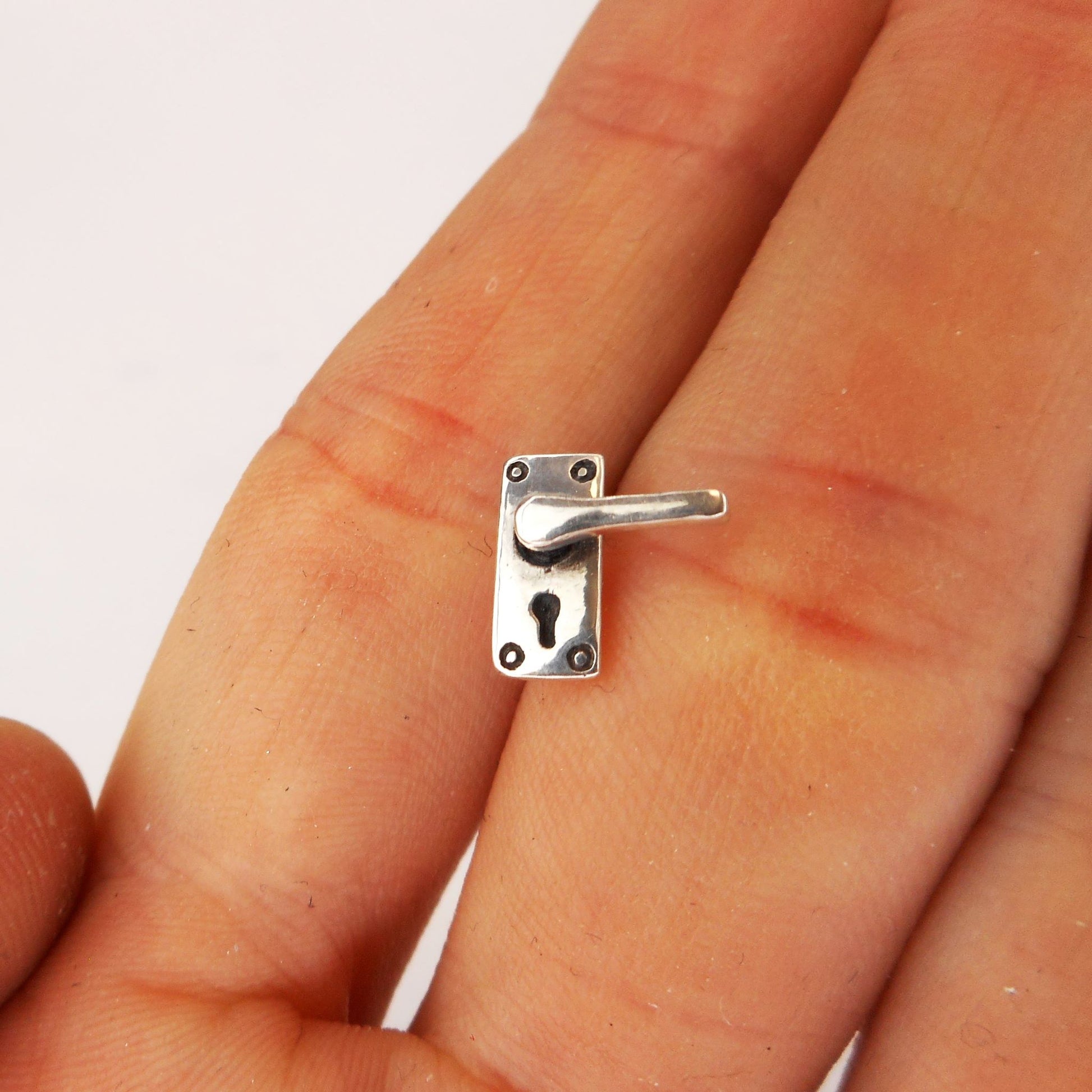 A photo of a miniature silver door handle, between two fingers of a hand.