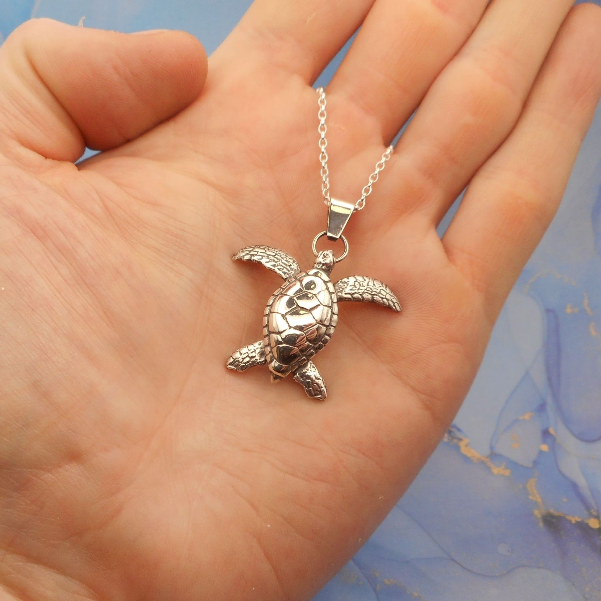 A photo of a turtle necklace on the palm of a hand.