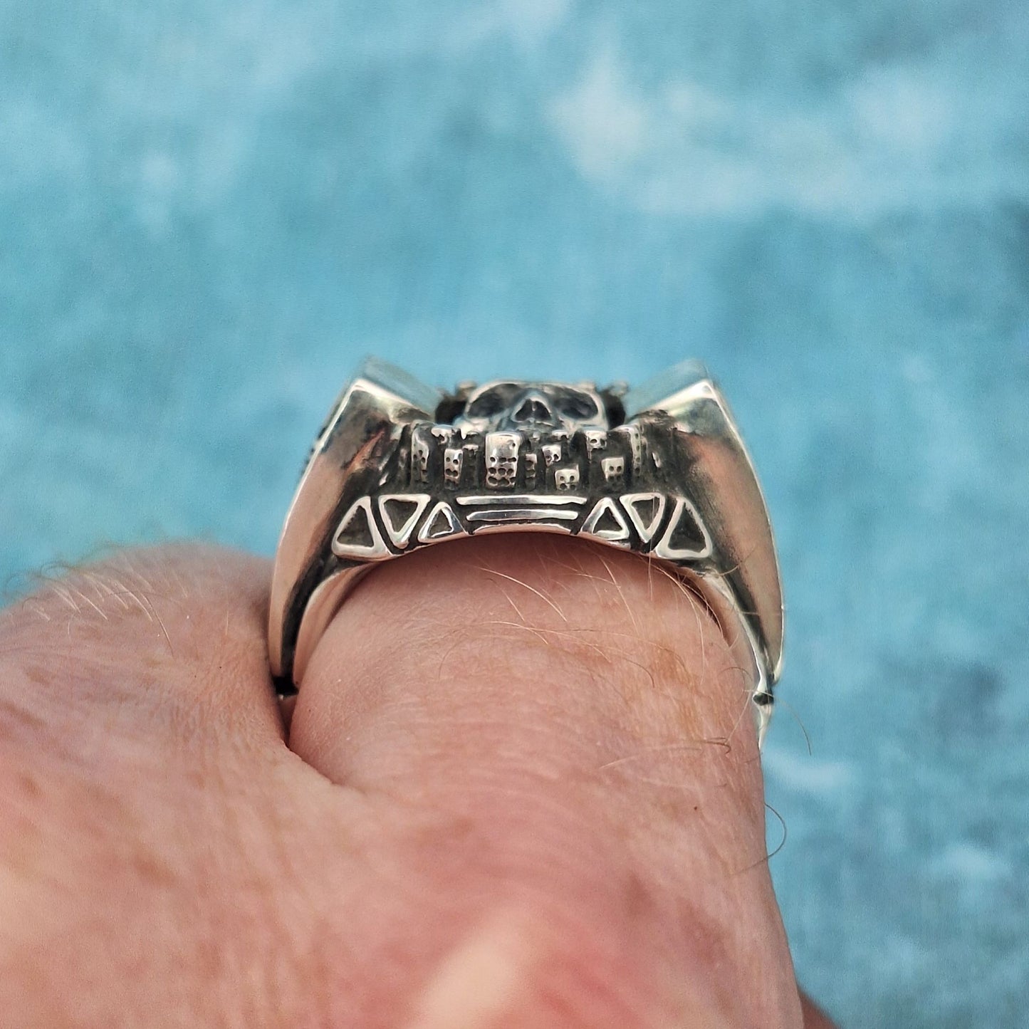 A photo of a large silver jewellery ring, featuring geometric shapes and a miniature city skyline, worn on an index finger.