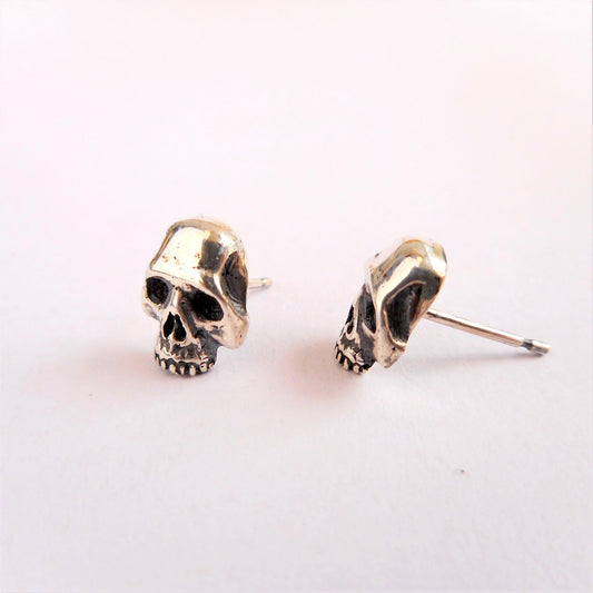 A photo of a pair of small silver skulls with earring stud attachments, on a white background.
