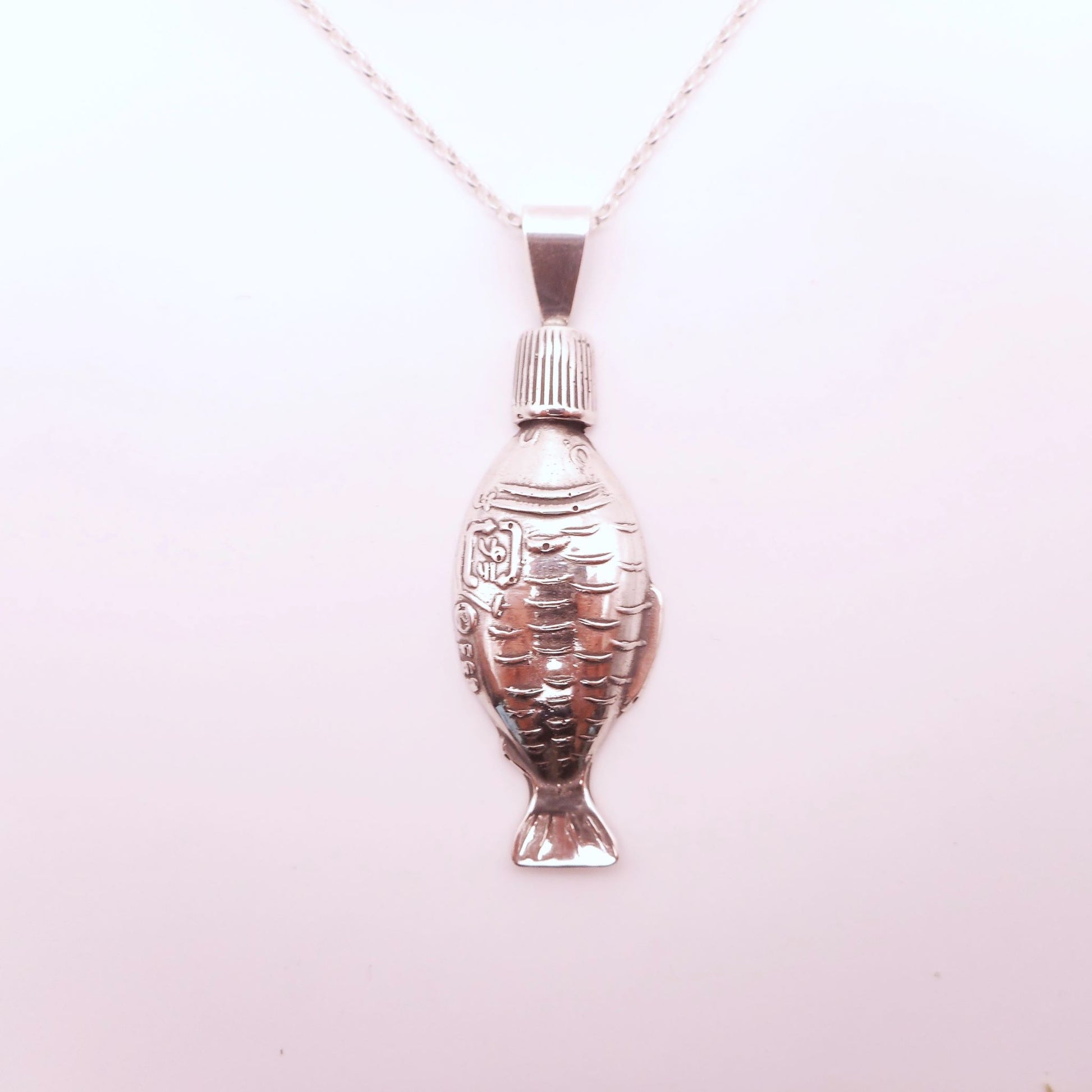 A photo of a soy sauce fish bottle made of silver, attached to a chain, on a white background.