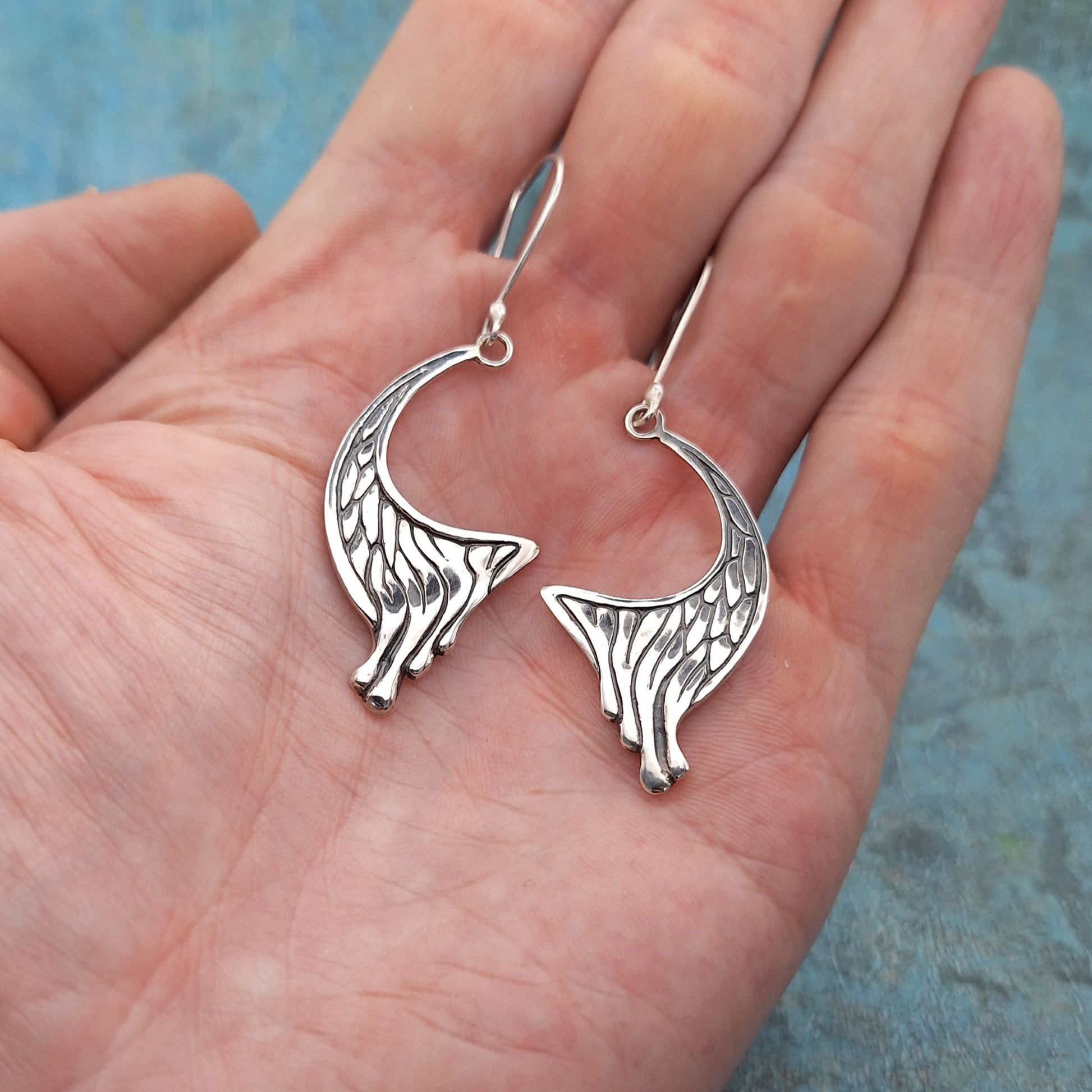 A photo of a pair of earrings shaped like they are leaking silver drips, resting on the palm of a hand.