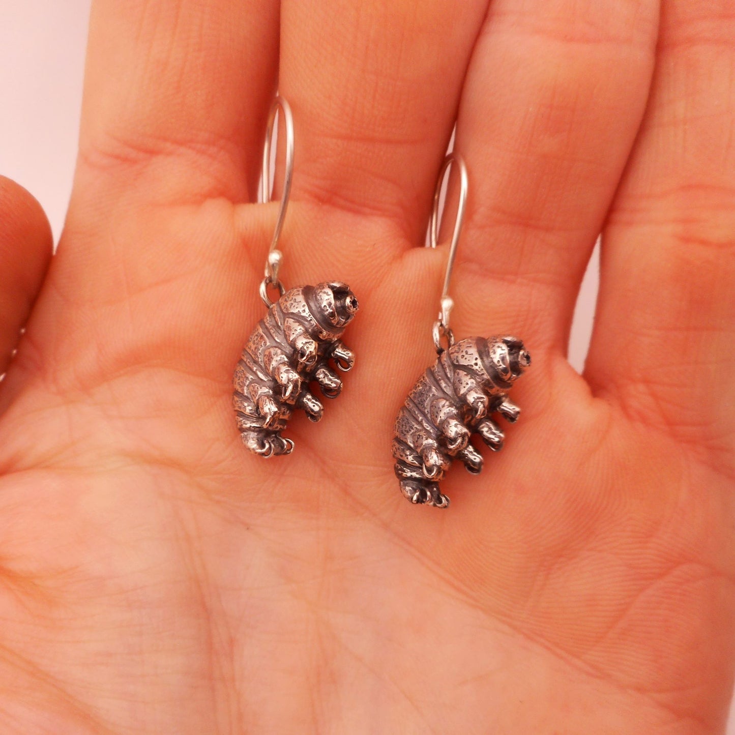 A photo of two tardigrade earrings made of silver, on the palm of a hand.
