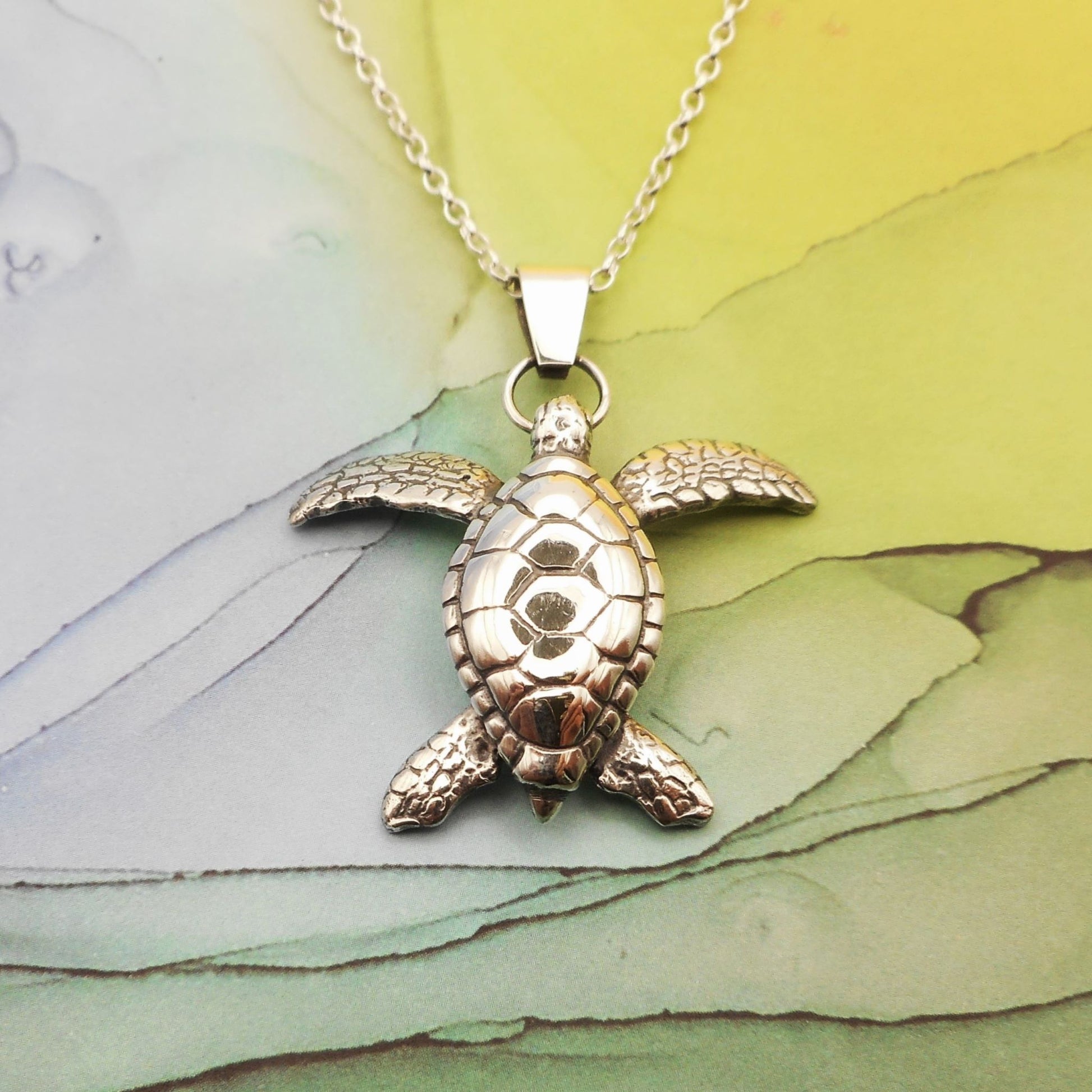 A photo of a silver pendant shaped like a turtle on a chain, on a multicoloured background.
