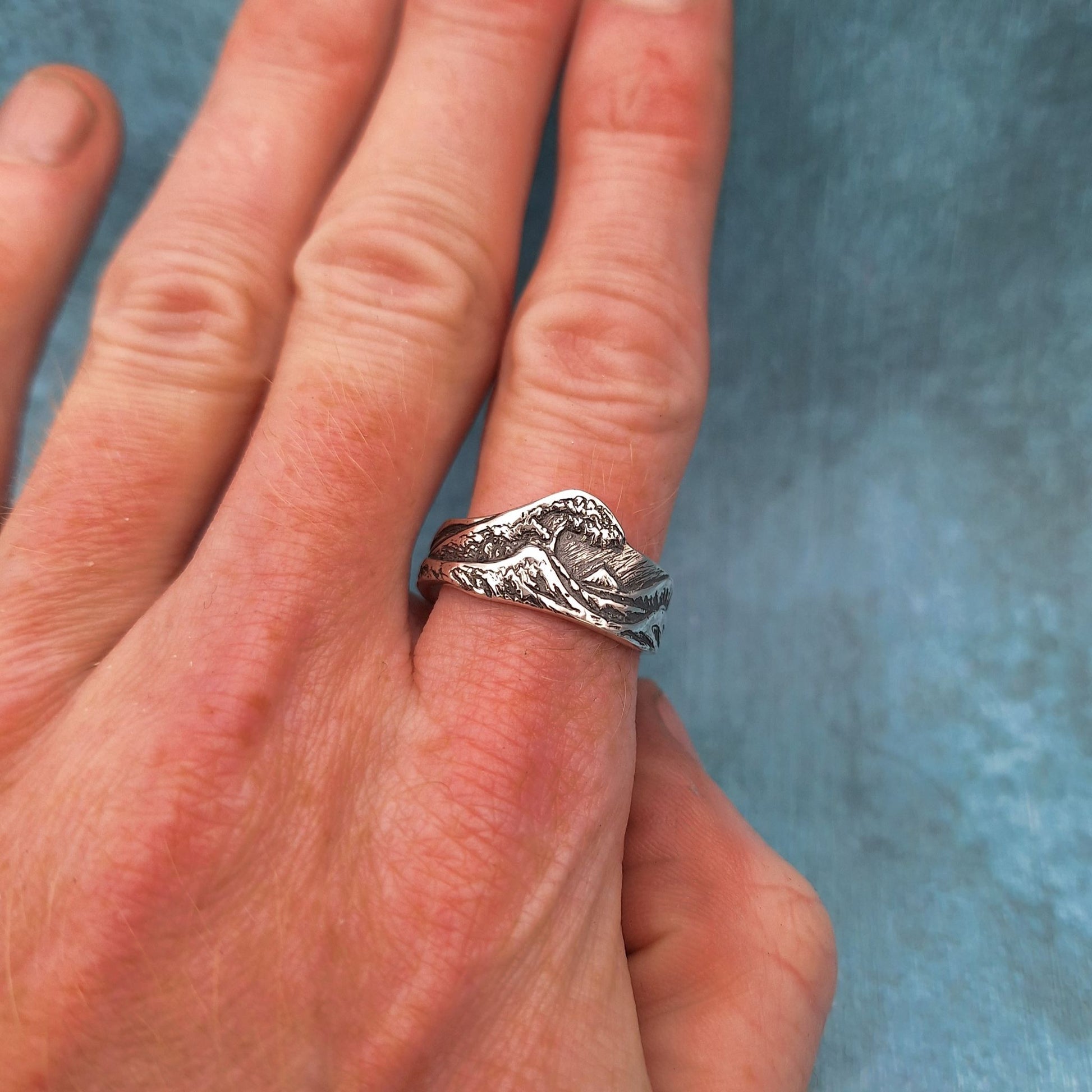 a wave ring worn on a finger, in front of a blue background.